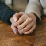 Quel message de soutien écrire pour la perte d'une maman ? Deux mains serrees ensemble sur une table en bois