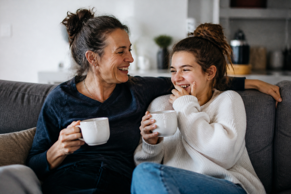 Mere et fille riant sur canape gris avec tasses
